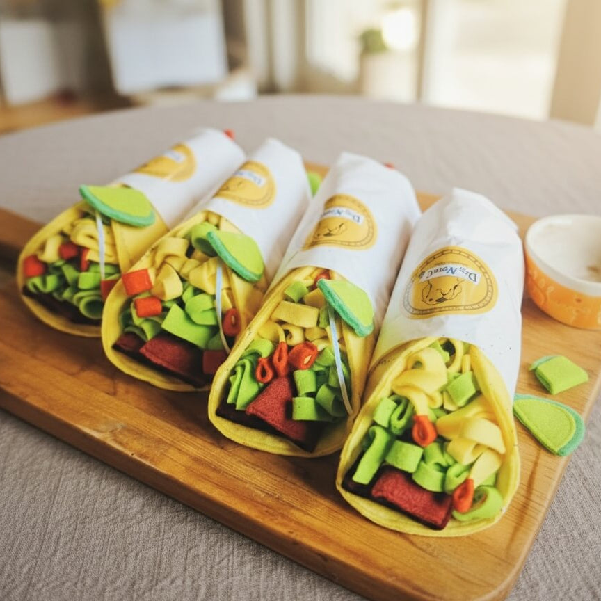 Présentation de plusieurs houets tapis de fouille pour chien en forme de tacos sur une planche en bois, mettant en valeur le design original avec faux avocat et viande.